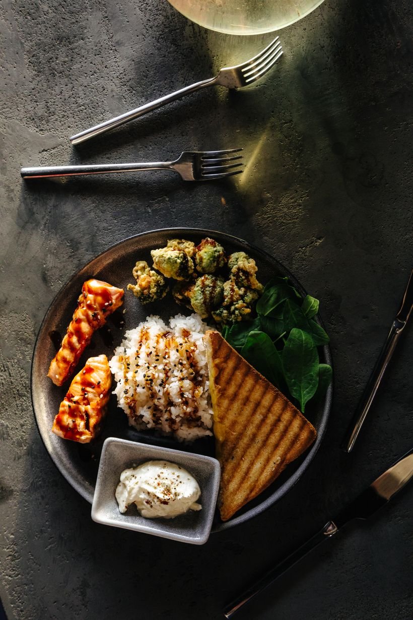 A high-protein meal of grilled salmon, rice and greens, shot from above on a dark slate surface